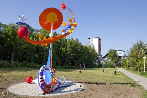 Von links: „Solarika“ mit ihren 19 sonnen- und windangetriebenen Bewegungen (600 x 450 x 254 cm) an ihrem neuen Platz auf dem Oberen Eselsberg; Künstlerin Claire Ochsner vor ihrem restaurierten Kunstwerk (Fotos: UK Ulm).